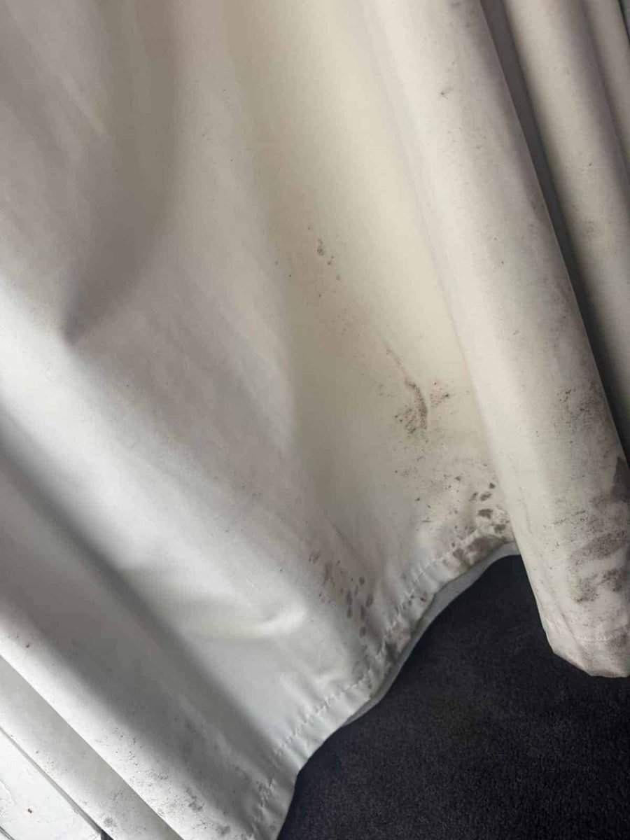 White curtain with black mould along the hem before cleaning